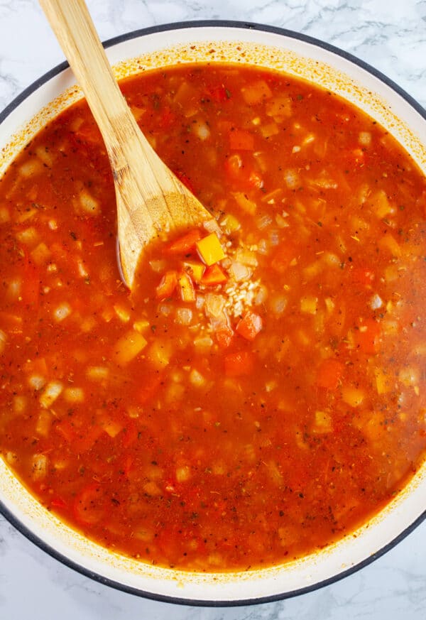 Uncooked Spanish rice with vegetable broth and tomato sauce in Dutch oven with wooden spoon.