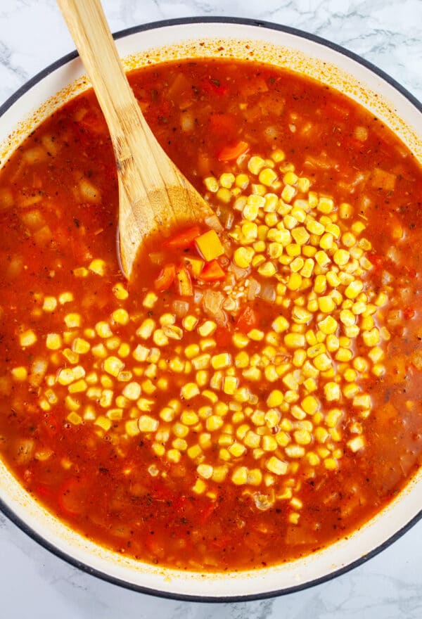 Uncooked Spanish rice with frozen corn in Dutch oven with wooden spoon.