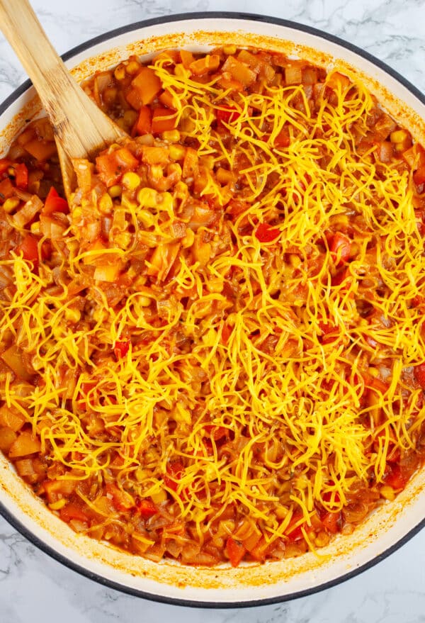 Cooked Mexican rice with shredded cheddar cheese in Dutch oven with wooden spoon.