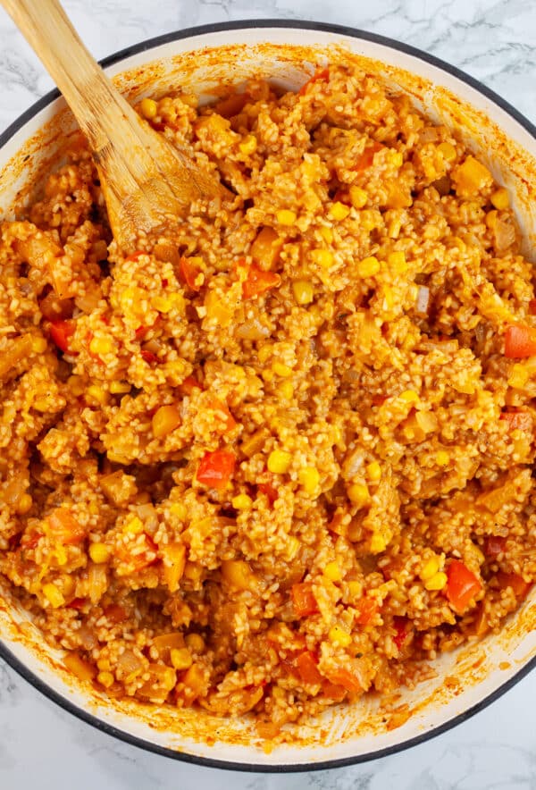 Cooked Spanish rice in Dutch oven with wooden spoon.
