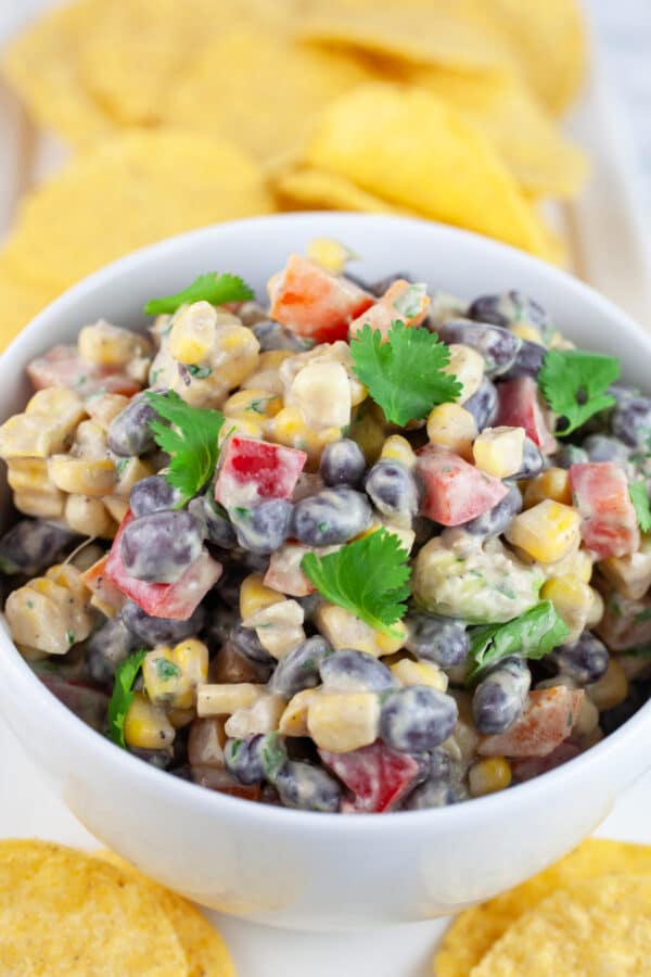 Southwest black bean corn salad in white bowl on serving platter with tortilla chips.