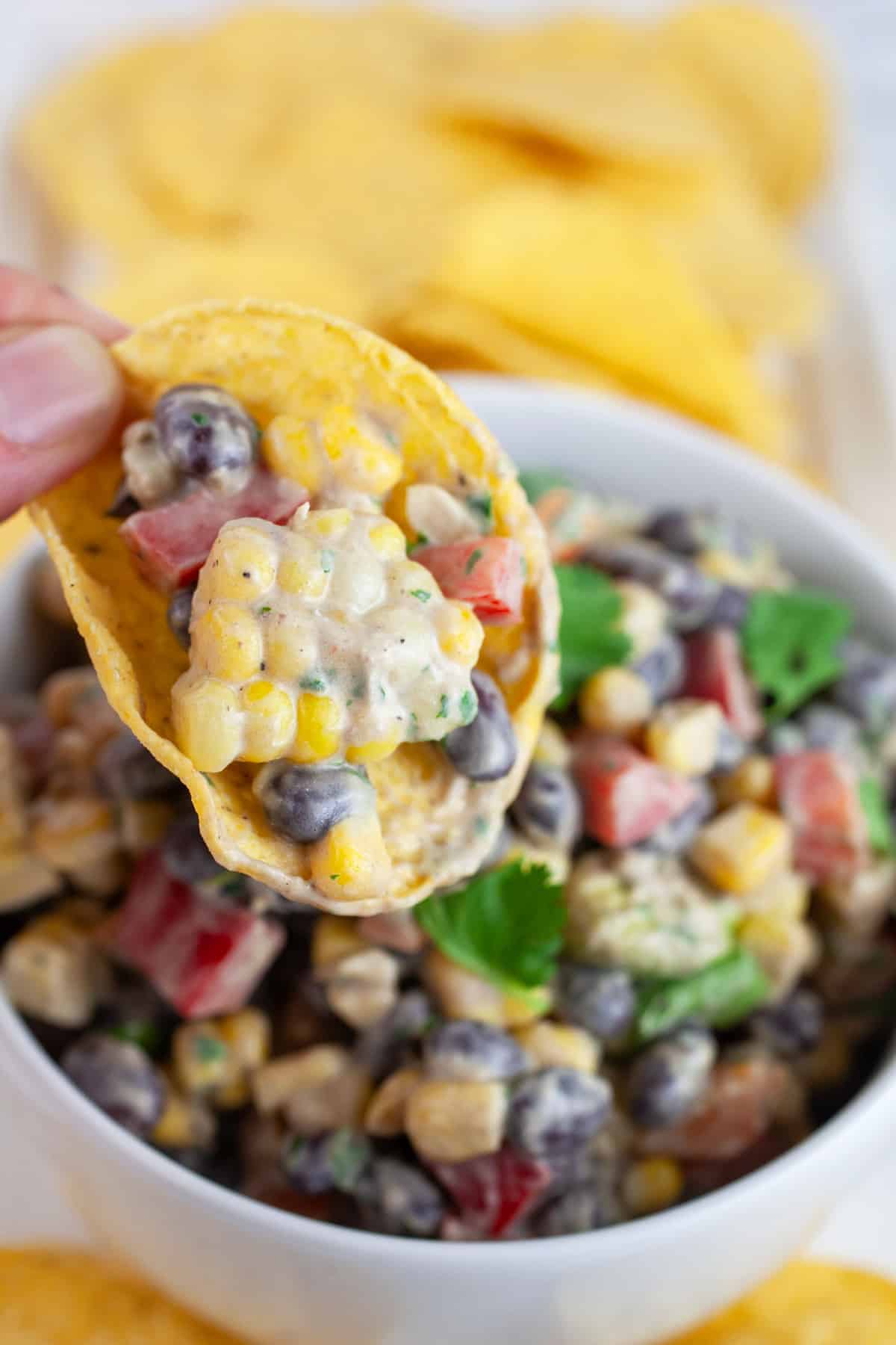 Southwest black bean corn salad on tortilla chip lifted from white bowl on platter.