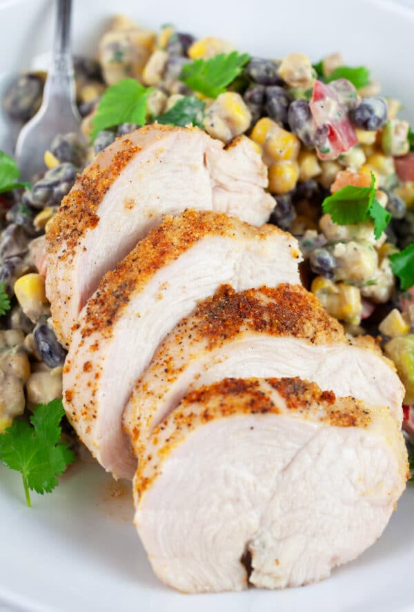Cooked, sliced chicken breasts and black bean corn salad in white bowl with fork.