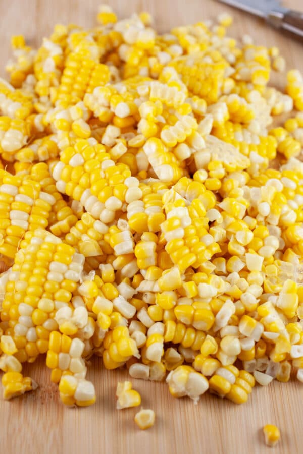 Sweet corn kernels on wooden cutting board with knife.