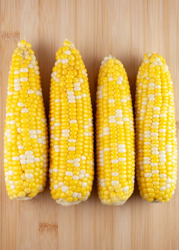 Cooked cobs of sweet corn on wooden cutting board.