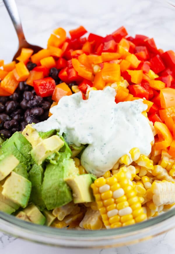 Dressing added to black bean corn salad in glass mixing bowl with spoon.