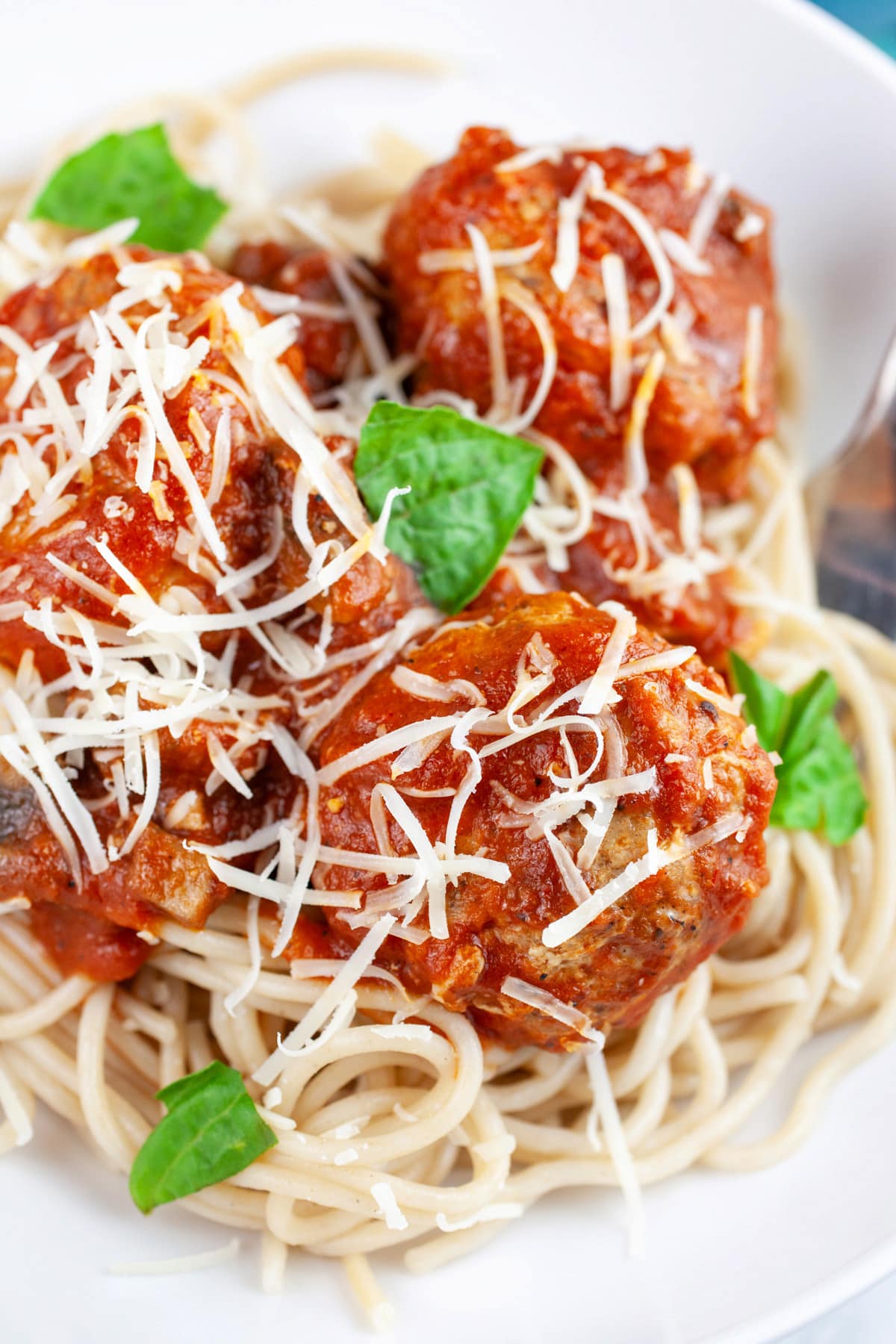 These Spaghetti and Turkey Meatballs make the best healthy comfort food recipe! These turkey meatballs are easy and homemade. Ground turkey is flavored with Italian spices and simmered in spaghetti or marinara sauce. I love the authentic flavors of this dish. This recipe is also gluten free! Perfect for a weeknight dinner or anytime. #meatballs #turkey #spaghetti #glutenfree Spaghetti and turkey meatballs garnished with Parmesan cheese and fresh basil in white bowl with fork.
