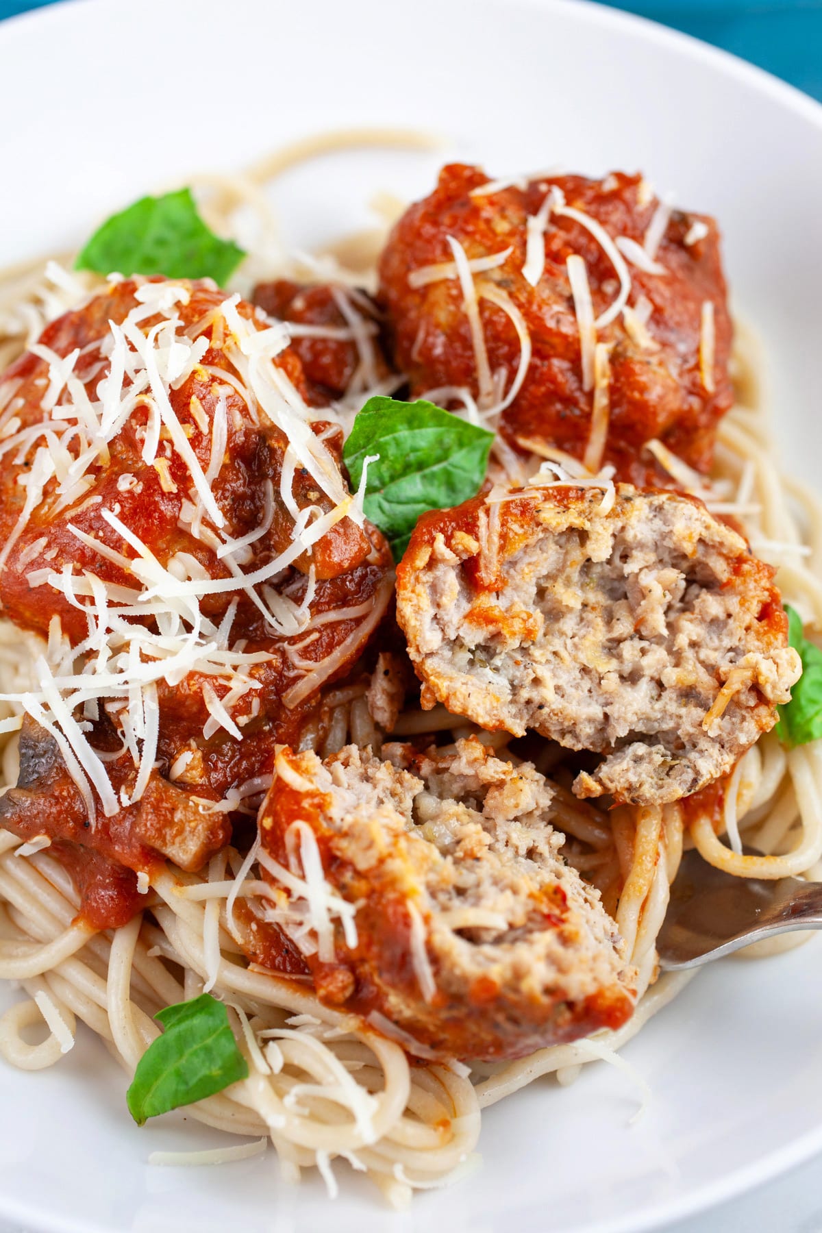 Turkey meatballs cut in half and spaghetti in white bowl with Parmesan cheese and fresh basil.