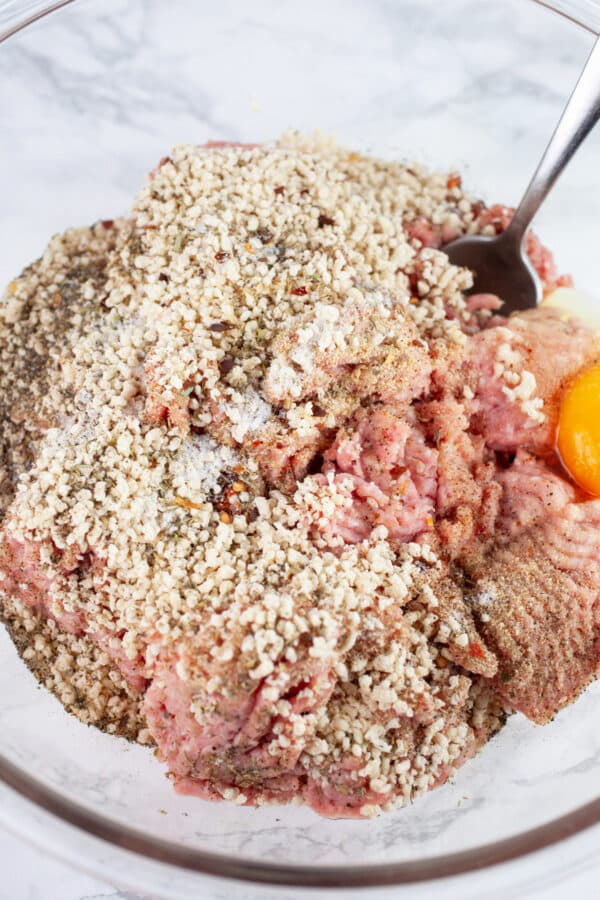 Ground turkey, breadcrumbs, egg, and spices in glass mixing bowl with spoon.