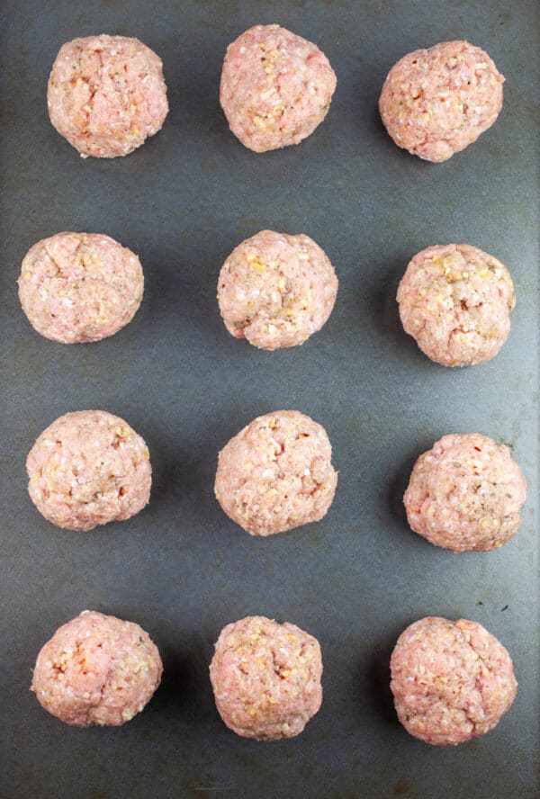 Uncooked ground turkey meatballs on baking sheet.