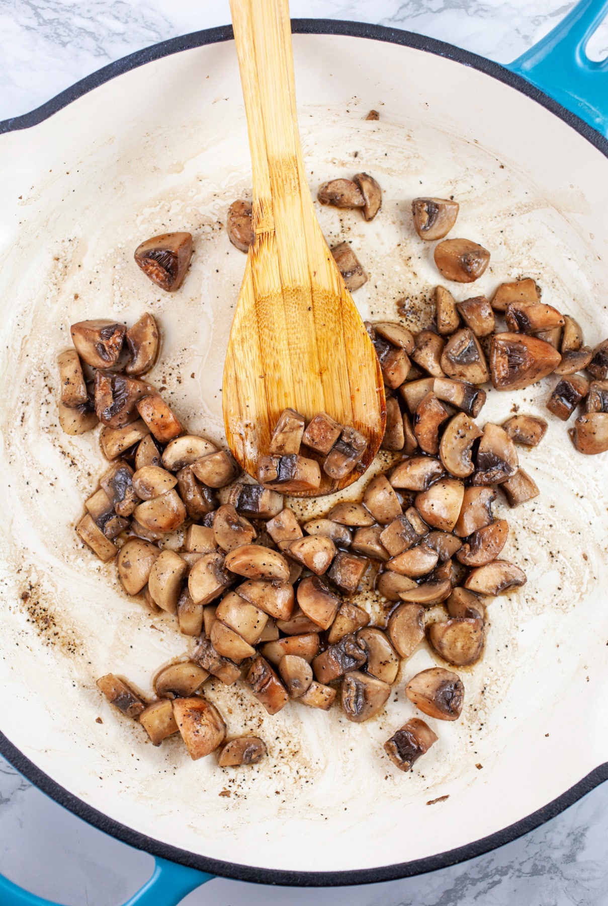 Diced mushrooms sauteed in skillet with wooden spoon.