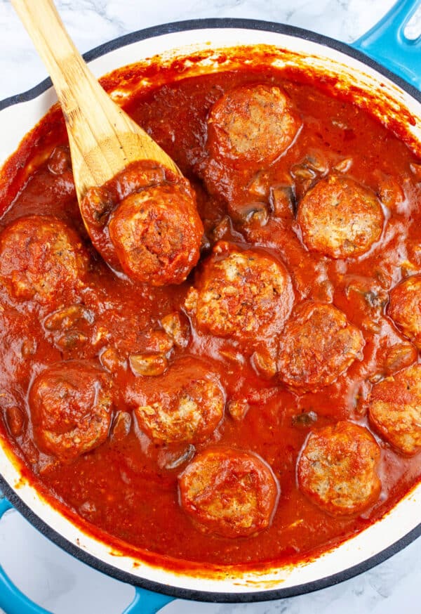 Turkey meatballs and mushrooms in marinara sauce in skillet with wooden spoon.