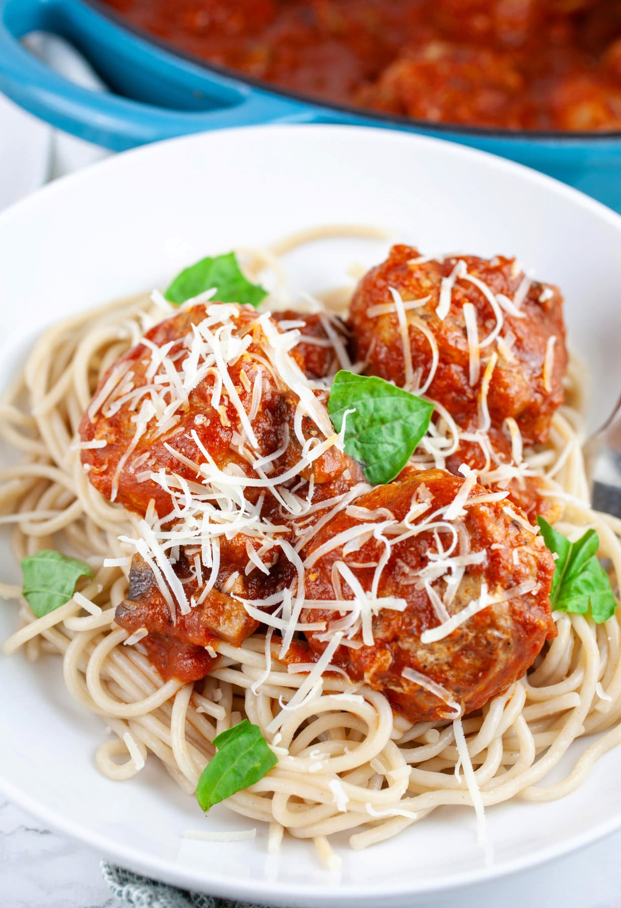 Spaghetti and turkey meatballs in white bowl garnished with Parmesan cheese and fresh basil.