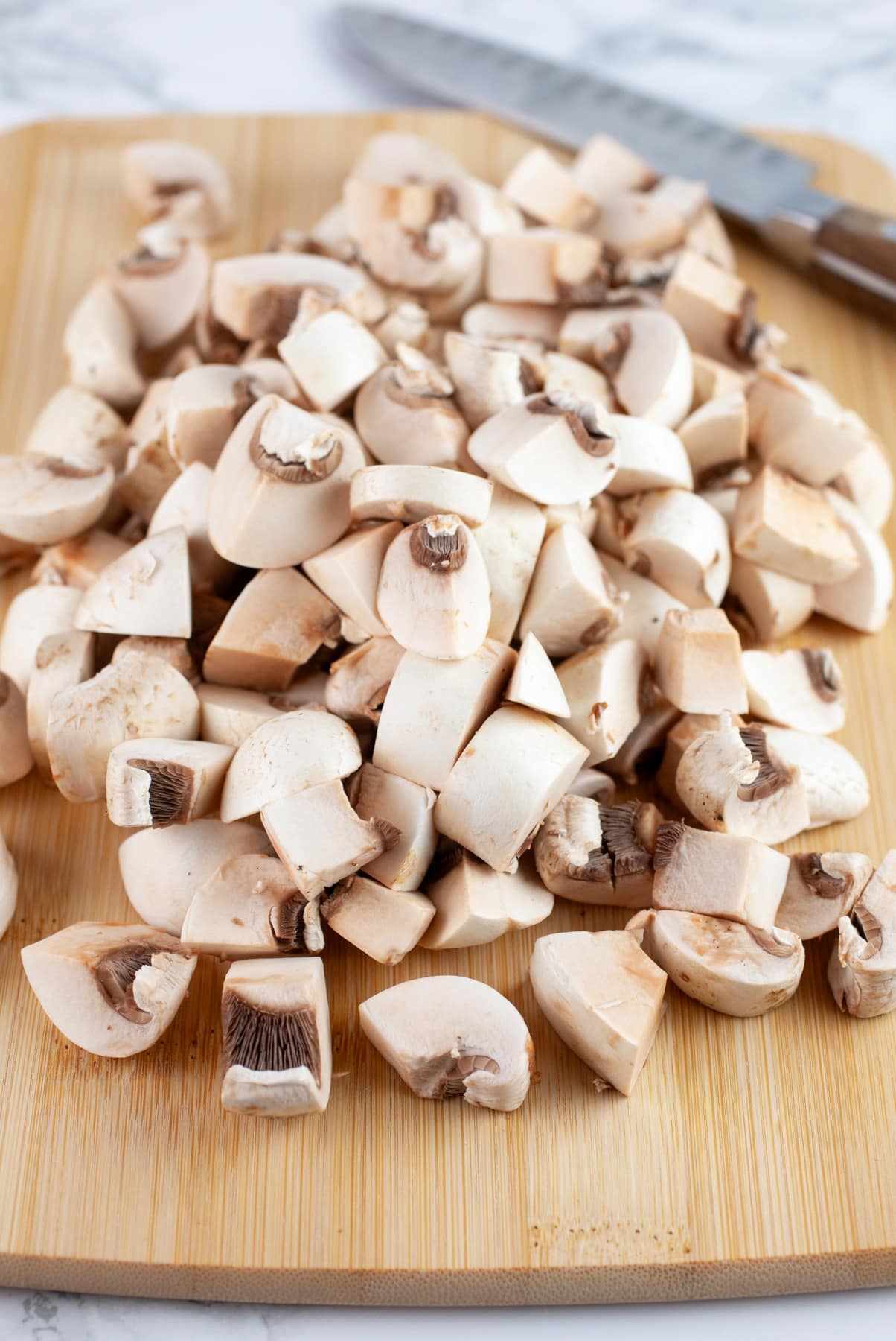 Diced mushrooms on wooden cutting board with knife.