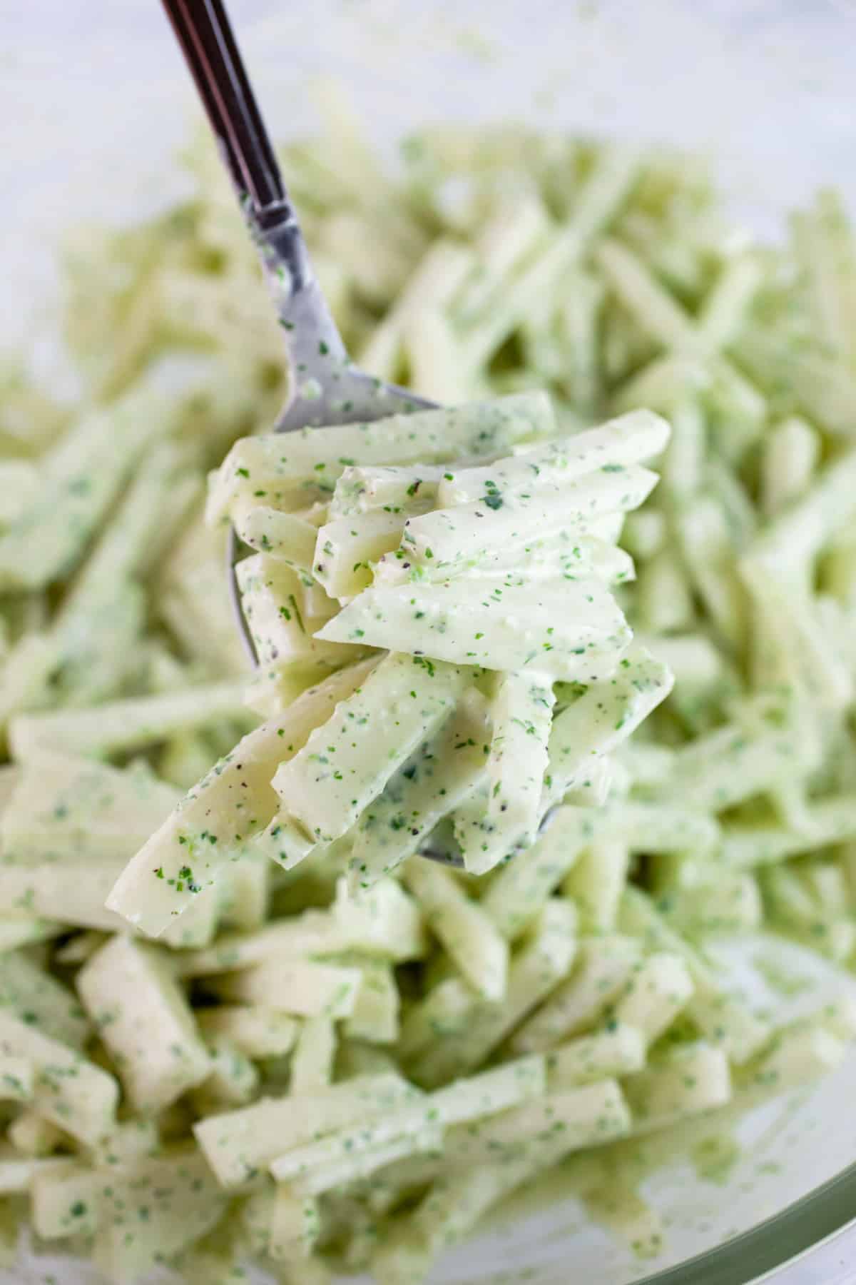 Spoonful of creamy cilantro lime kohlrabi slaw lifted from glass bowl.