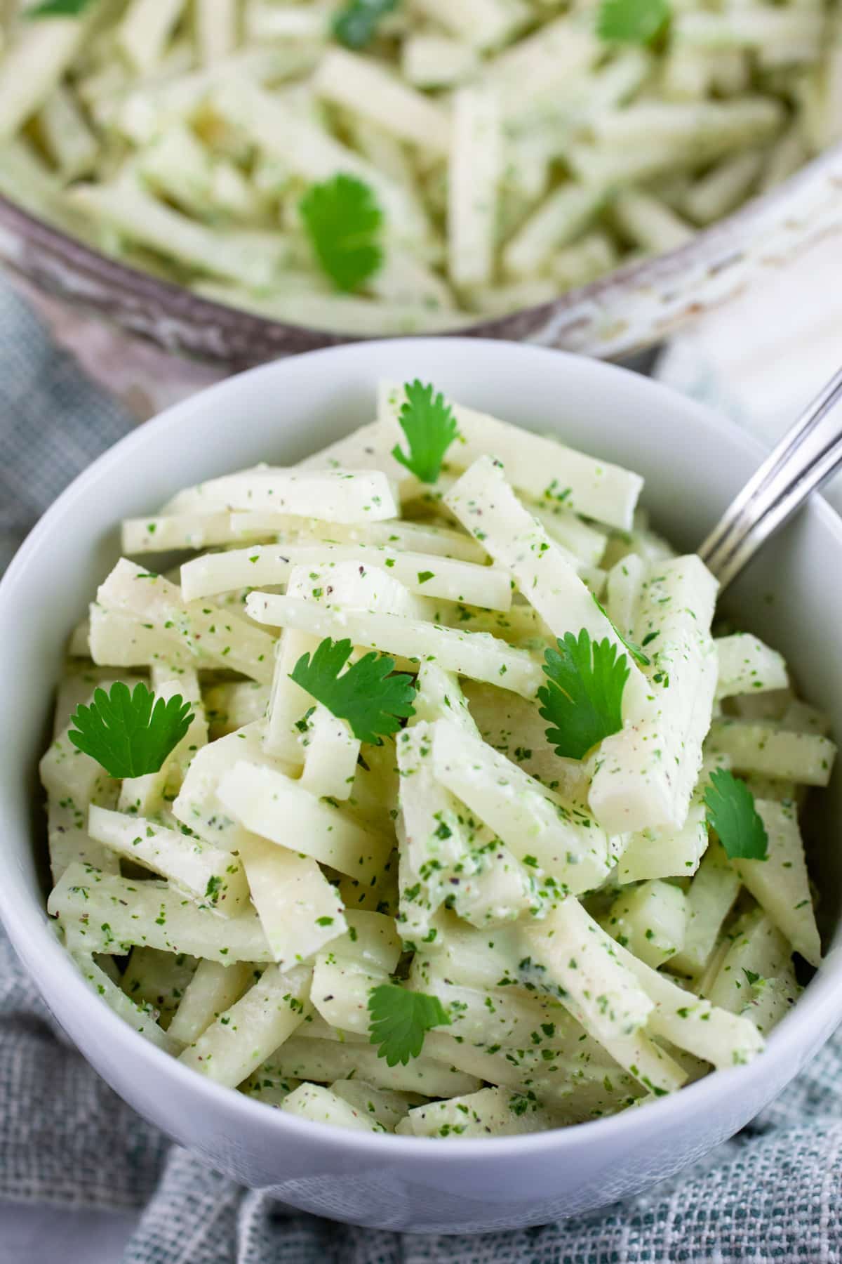 Kohlrabi coleslaw garnished with fresh cilantro in white bowl with fork.