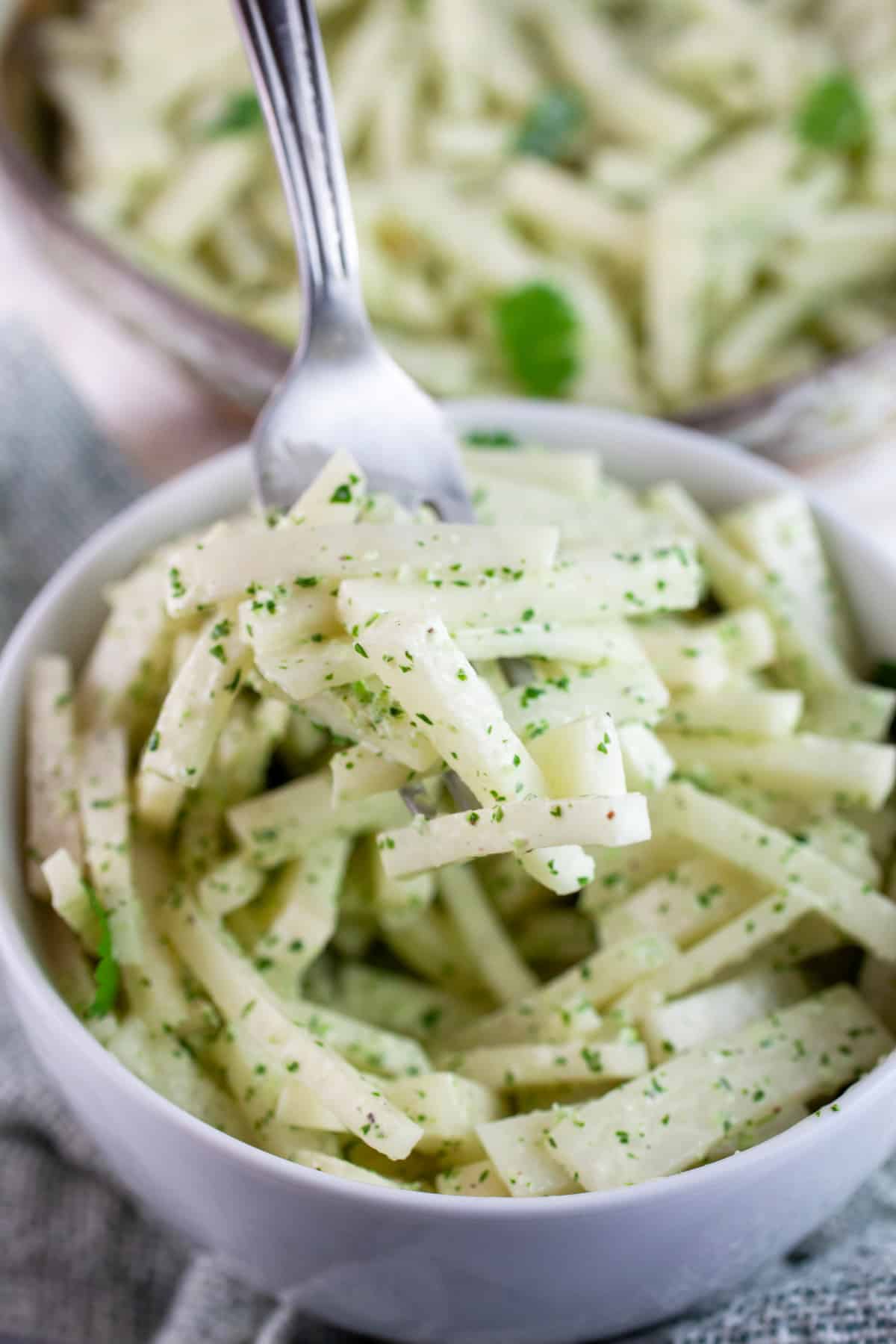Forkful of kohlrabi slaw lifted from white bowl.