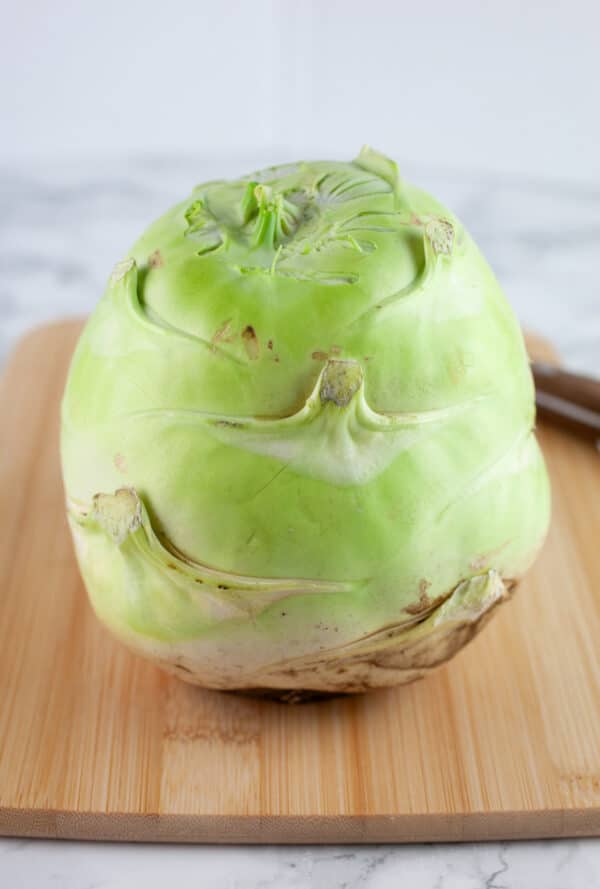 Whole kohlrabi without leaves on wooden cutting board.
