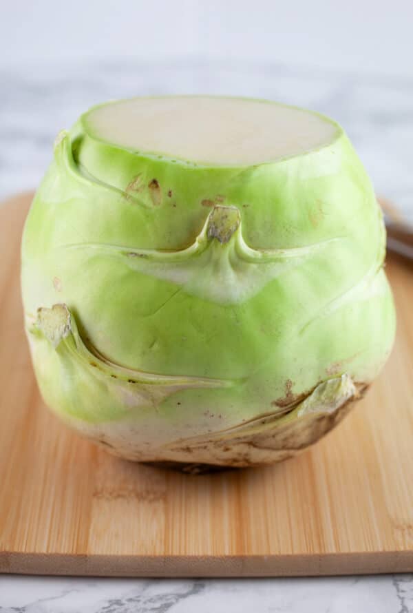 Kohlrabi with top and bottom cut off on wooden cutting board.