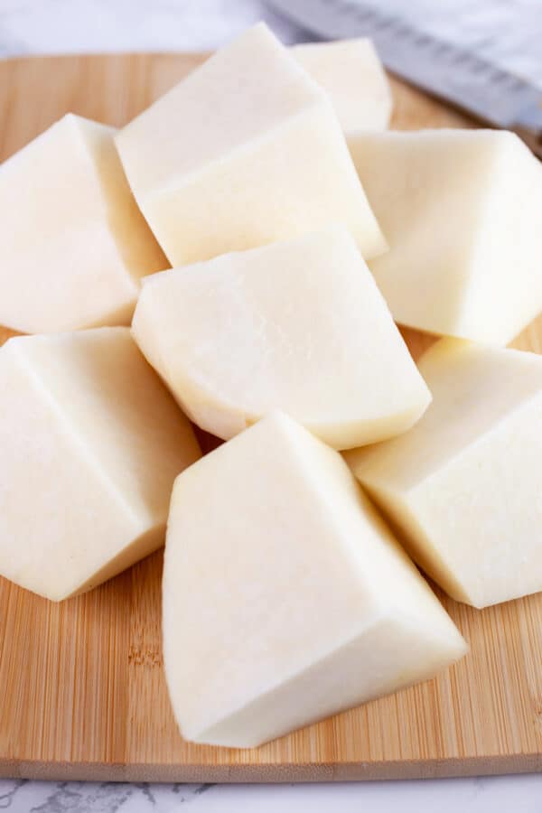 Kohlrabi cut into chunks on wooden cutting board.