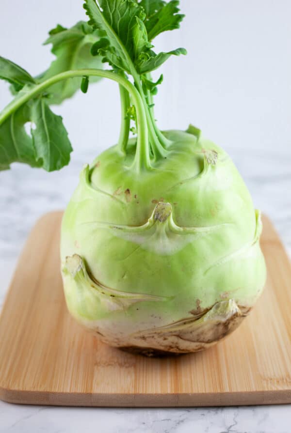 Whole kohlrabi with leaves on wooden cutting board.