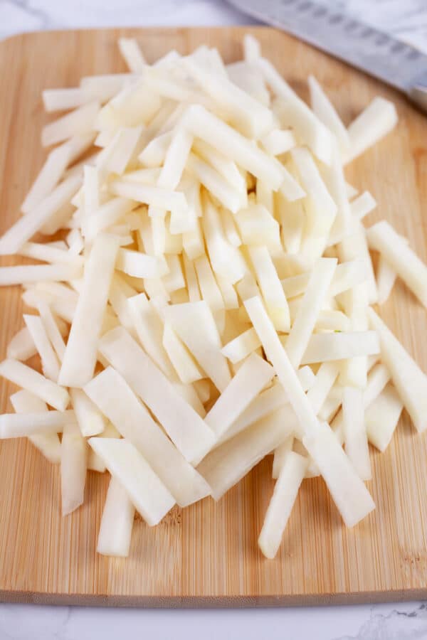 Kohlrabi matchsticks on wooden cutting board with knife.