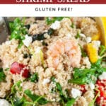 Quinoa zucchini shrimp salad with arugula in ceramic bowl garnished with lemon wedge.