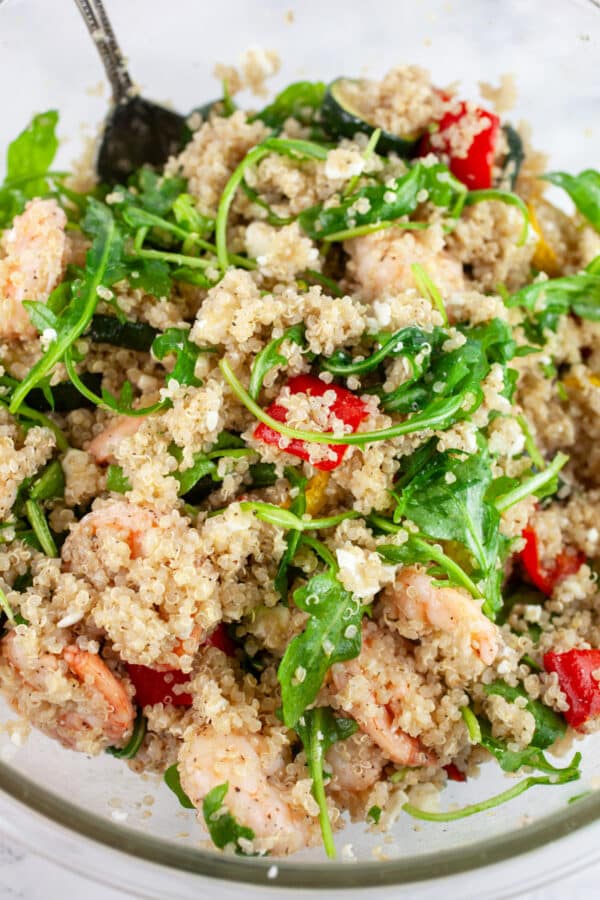 Quinoa shrimp zucchini salad with arugula in glass mixing bowl with spoon.