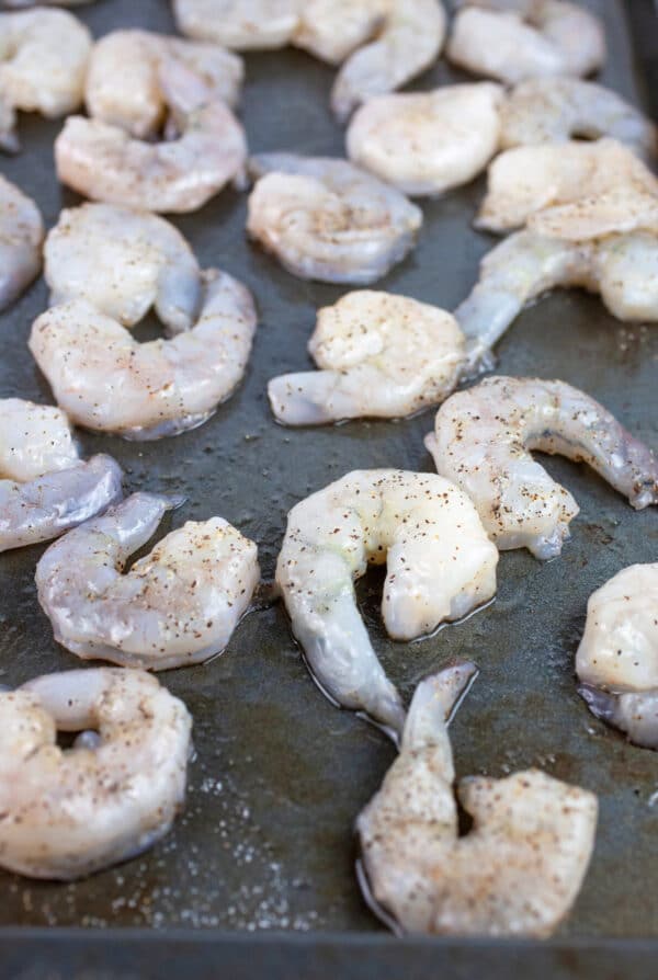 Raw shrimp tossed in olive oil, salt and pepper on baking sheet.