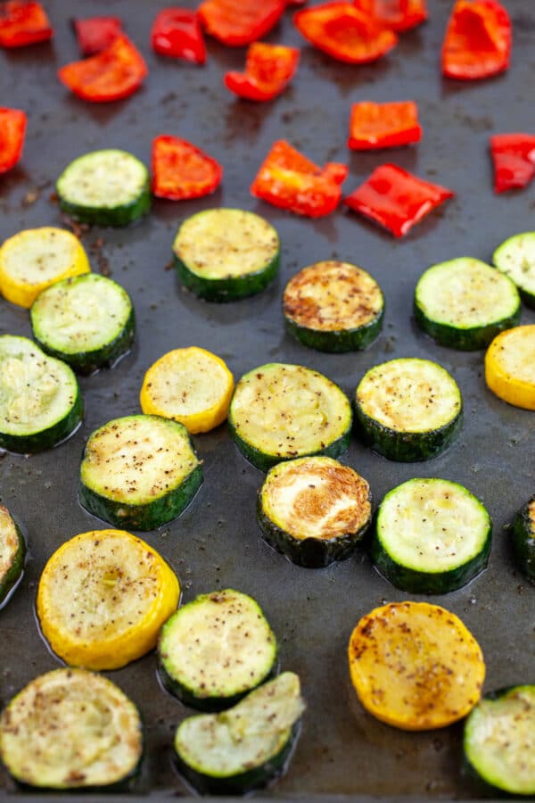 Roasted zucchini, summer squash, and red bell peppers on baking sheet.