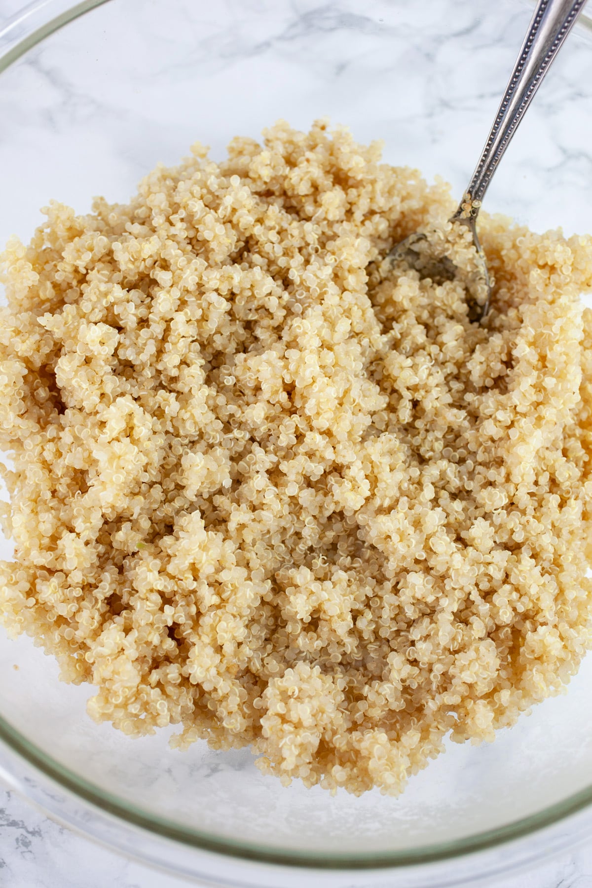 Cooked quinoa in large glass bowl with spoon.