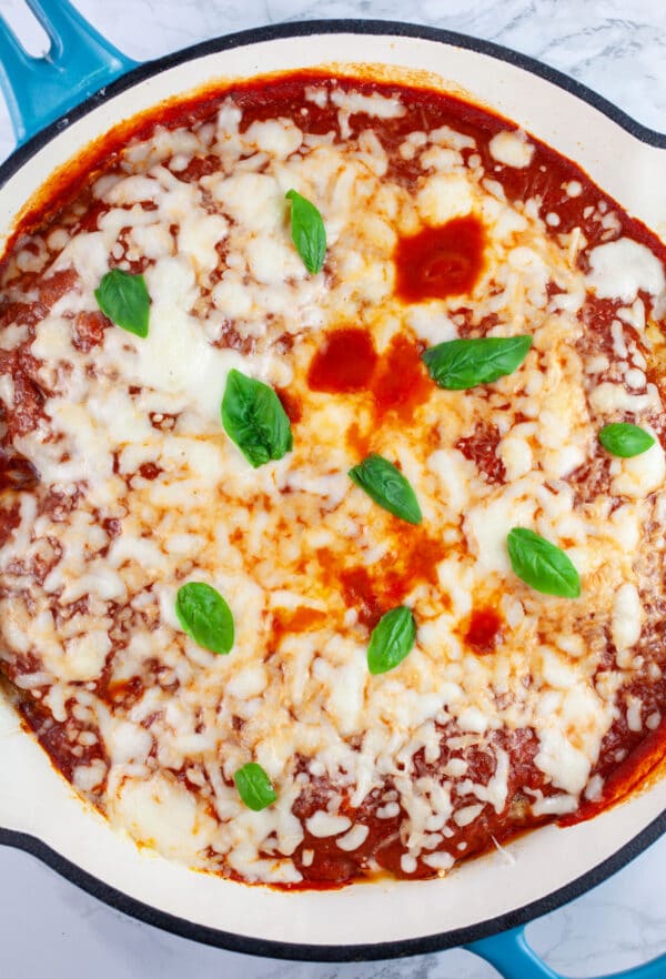 Chicken Parmesan garnished with basil in cast iron skillet.