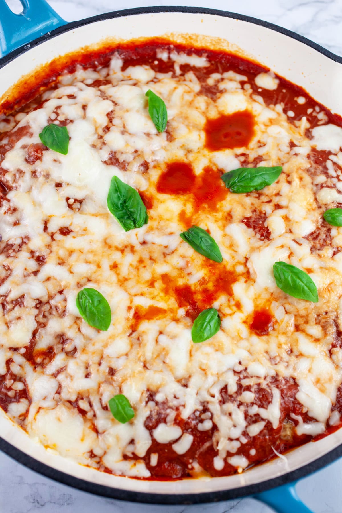 Chicken Parmesan garnished with basil in cast iron skillet.