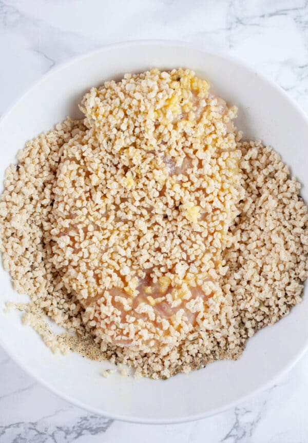 Raw chicken breast coated in Panko breadcrumbs in white bowl.
