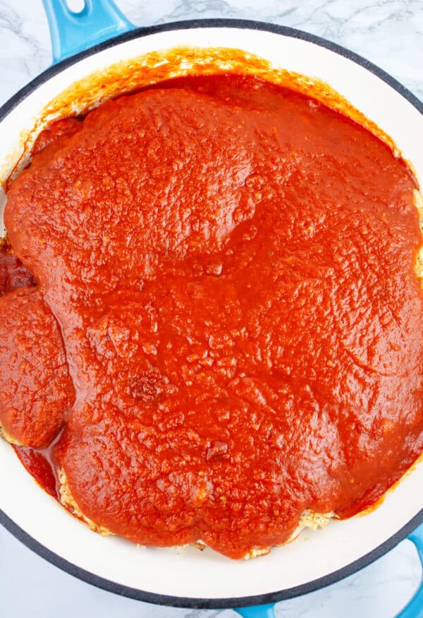 Uncooked chicken Parmesan with marinara sauce in cast iron skillet.