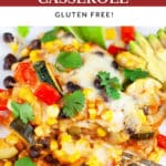 Vegetarian enchilada casserole on white plate with fork garnished with fresh cilantro, sliced avocado, and lime wedges.