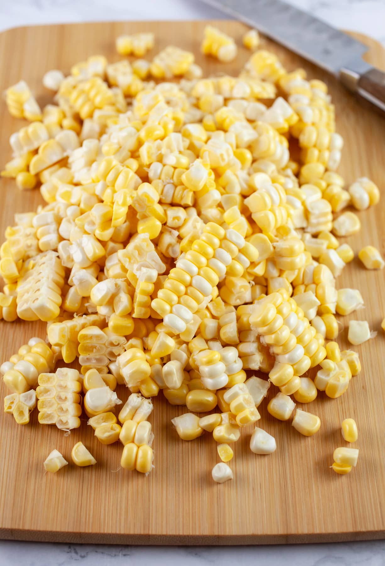 Sweet corn kernels on wooden cutting board with knife.