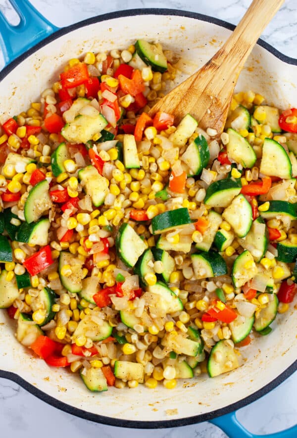 Chopped vegetables sauteed in ceramic cast iron skillet with wooden spoon.