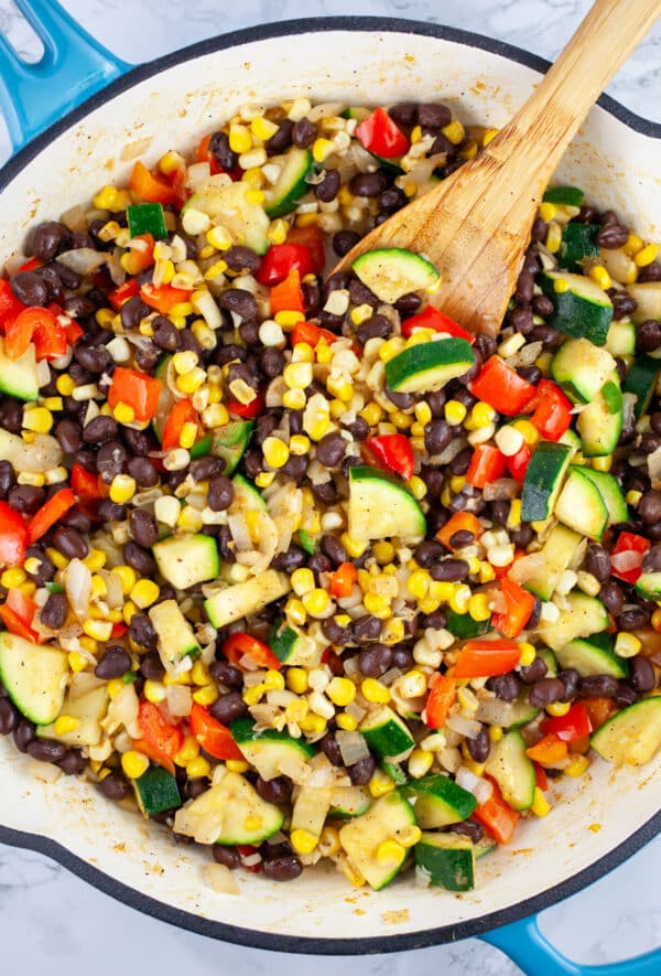 Chopped vegetables and black beans sauteed in ceramic cast iron skillet with wooden spoon.