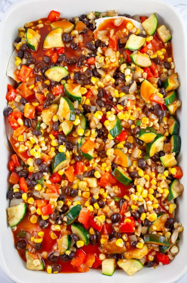 Sauteed vegetables and red enchilada sauce in ceramic casserole dish.