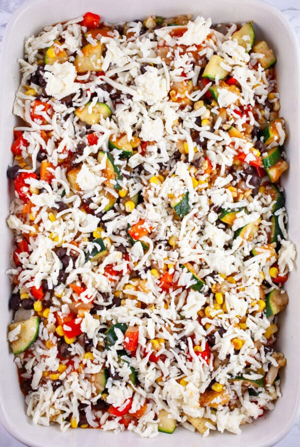 Uncooked enchilada casserole with shredded mozzarella cheese in ceramic casserole dish.