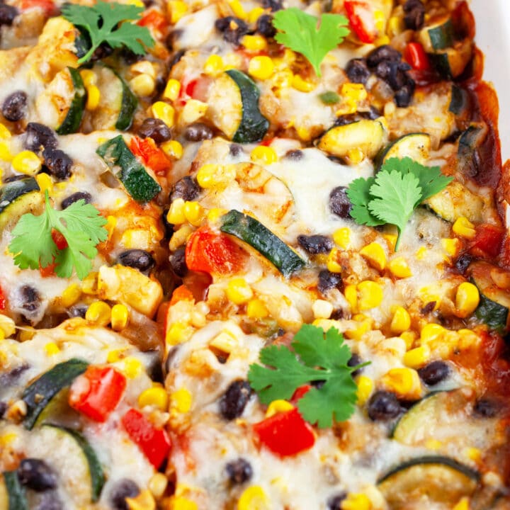 Vegetarian enchilada casserole garnished with fresh cilantro in ceramic casserole dish.