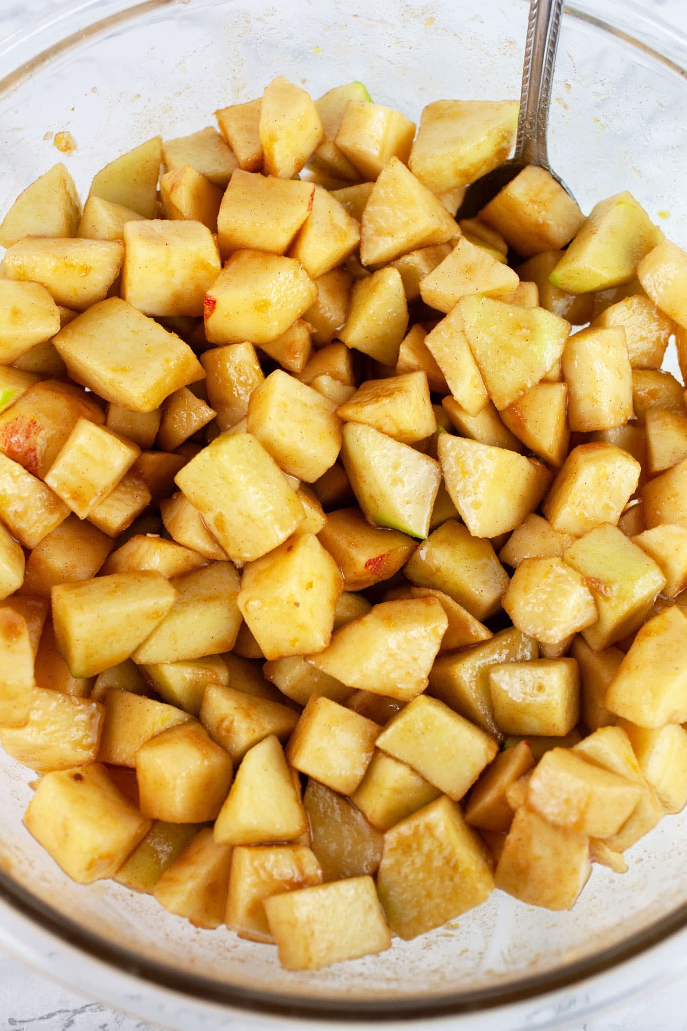 Diced apples with spices in large glass bowl with spoon.