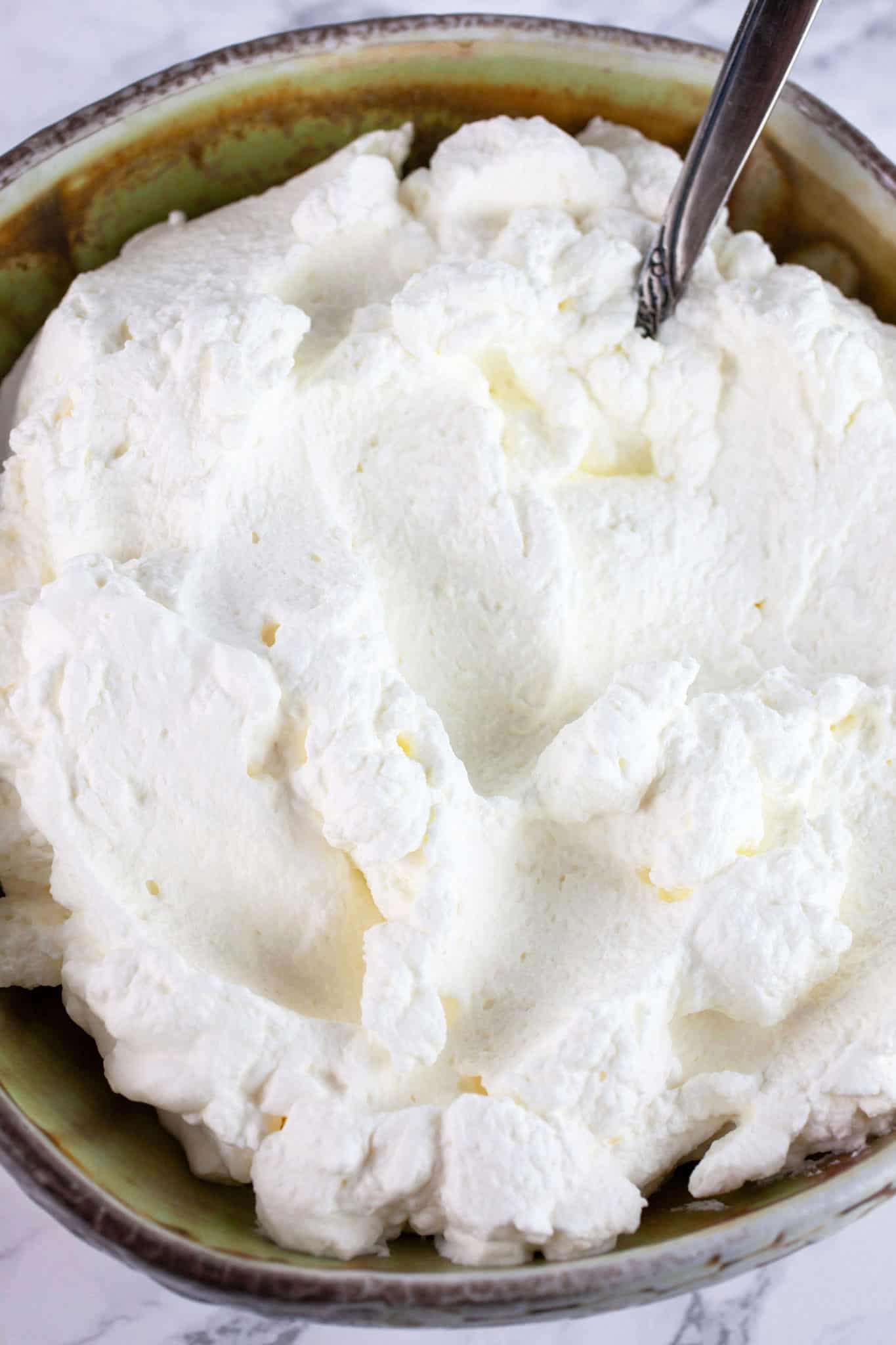 Homemade whipped cream in ceramic bowl with spoon.