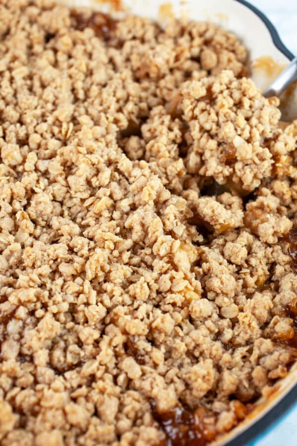 Baked apple crisp with streusel in cast iron skillet with large spoon.