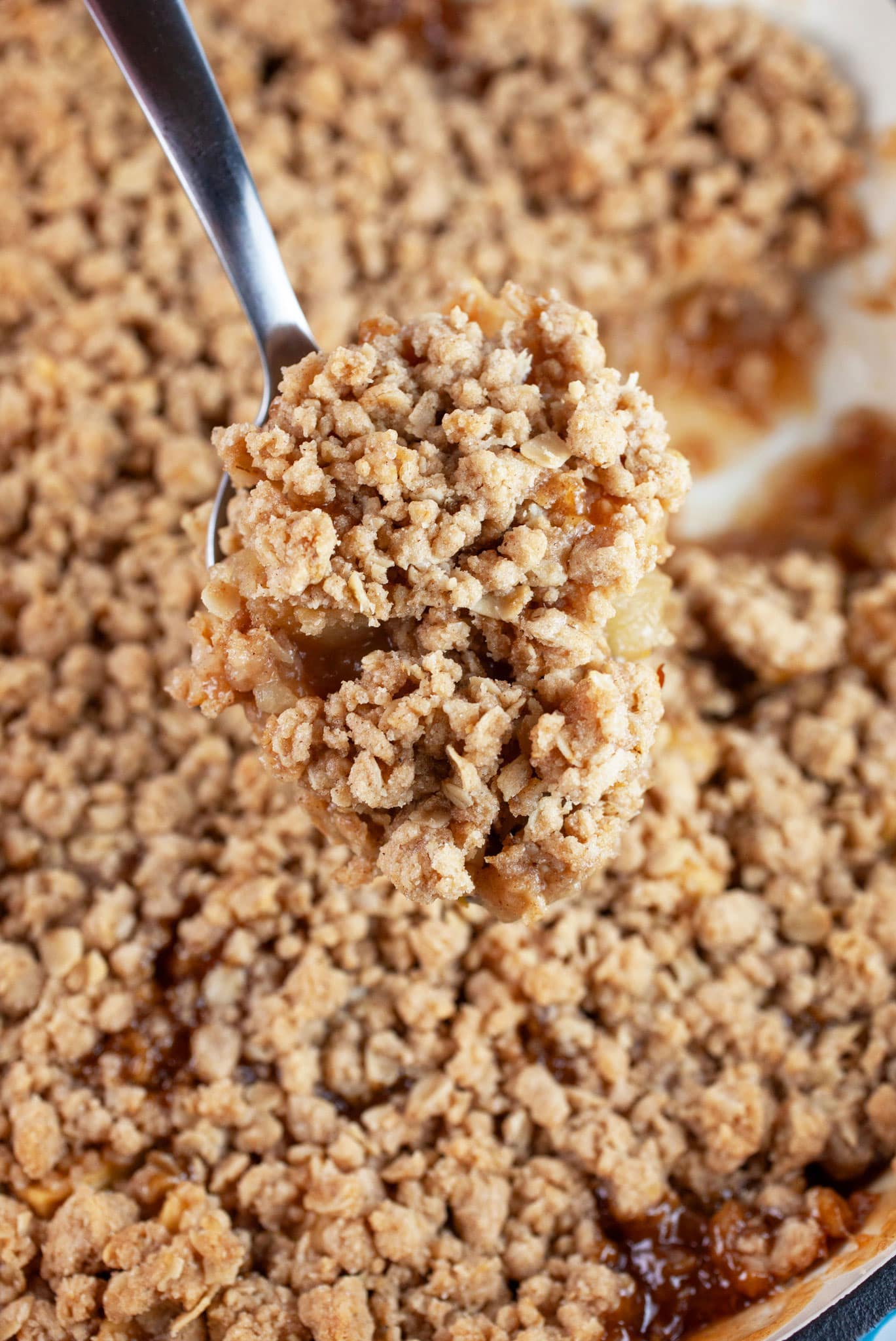 Scoop of apple crisp lifted from cast iron skillet on metal spoon.