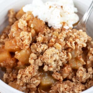Gluten free apple crisp with whipped cream in white bowl with fork.