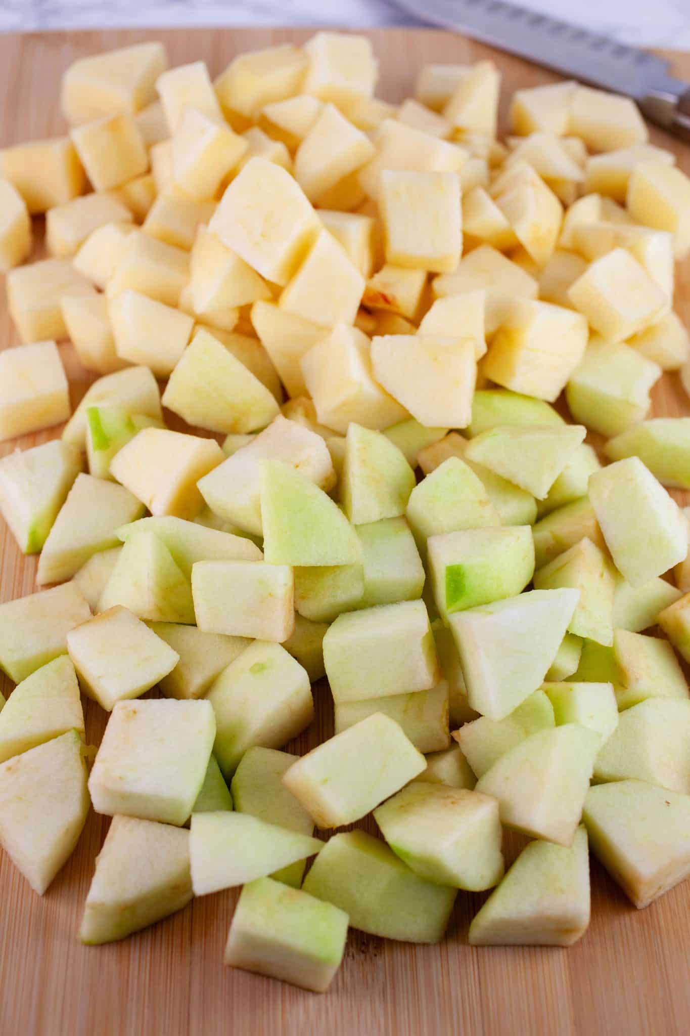 Diced, unpeeled Granny Smith and Gala apples on wooden cutting board with knife.
