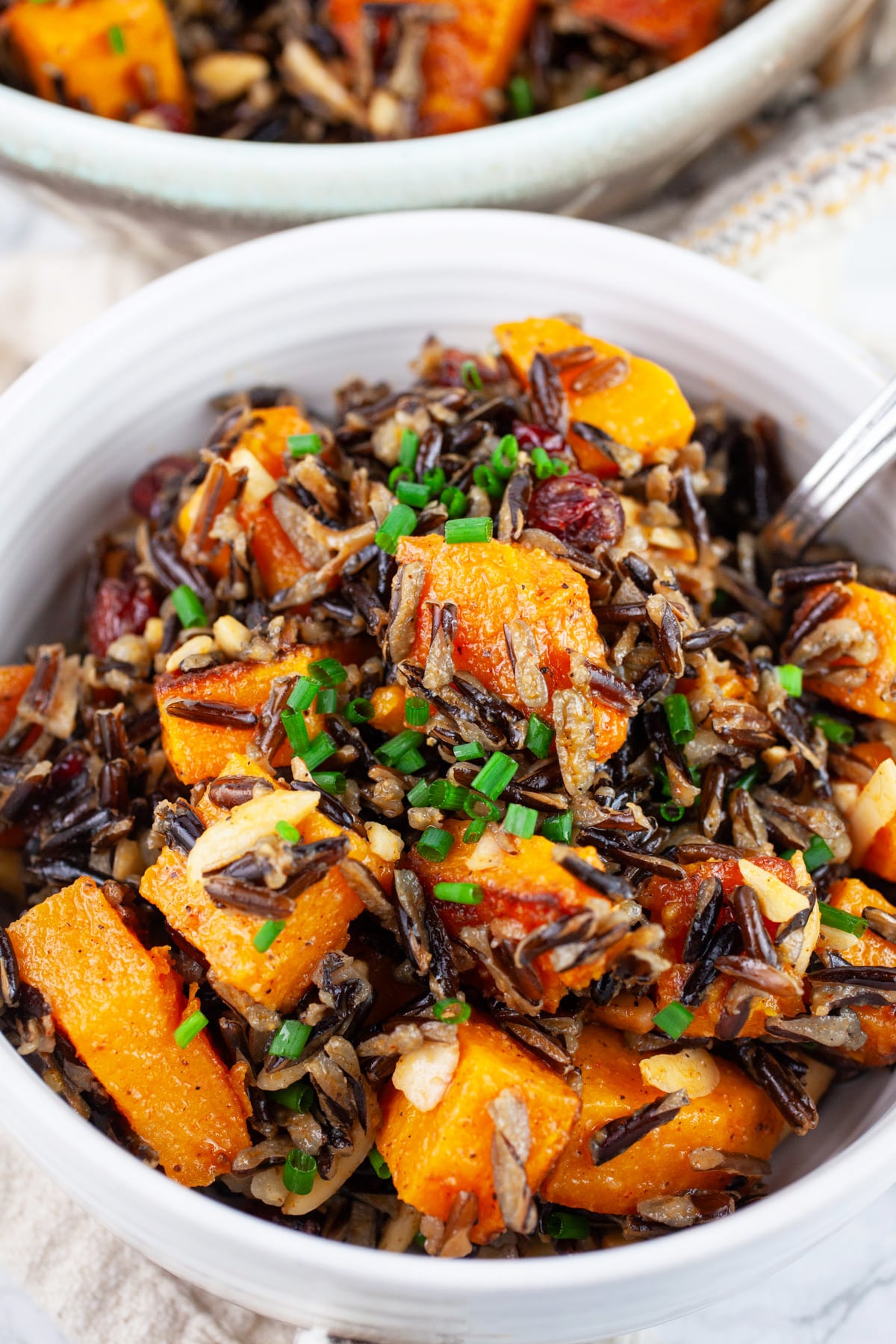 Wild rice butternut squash salad in white bowl with fork garnished with minced chives.