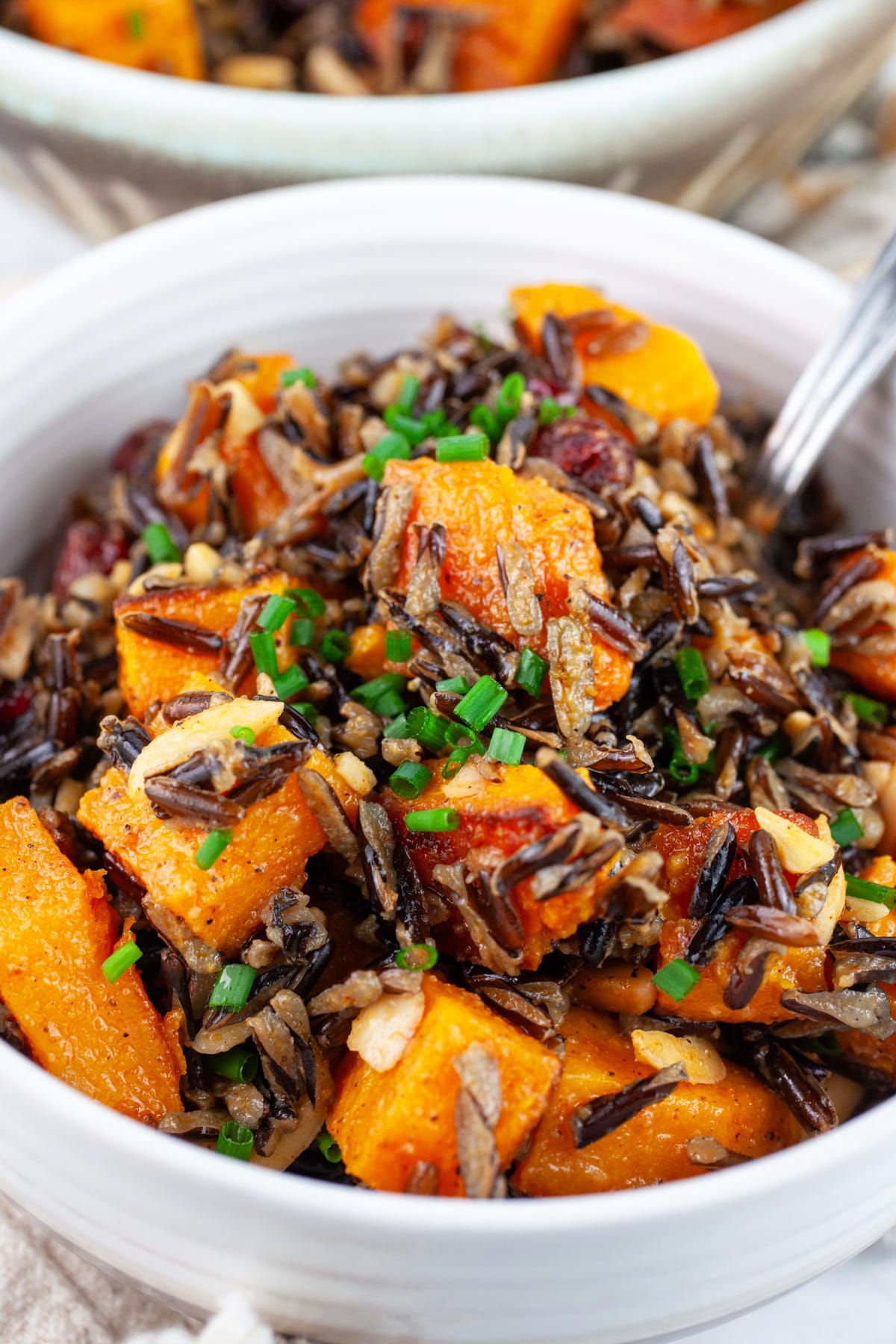 Wild rice butternut salad in white bowl with spoon garnished with minced chives.